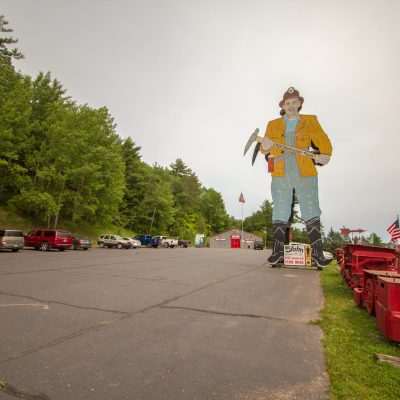 Mining tour sign with giant miner statue and flags.